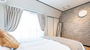 Un dormitorio moderno con una cama grande, cortinas color beige, un reloj en la pared y suelo de madera.