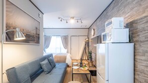 Un espacio habitable compacto con sofá, mesa de comedor, una pequeña cocina con microondas y un cuadro en la pared.