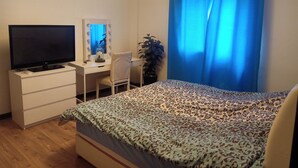 Une chambre à coucher avec un lit, un bureau avec une télévision, une chaise, un miroir et une fenêtre avec des rideaux bleus.
