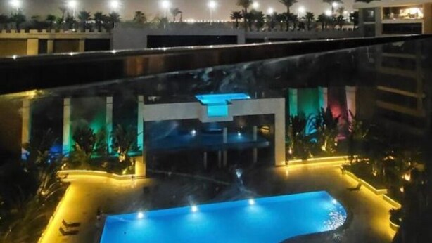 Vue nocturne d’une piscine sur le toit, avec un ciel dégagé, une piscine illuminée et les bâtiments environnants.