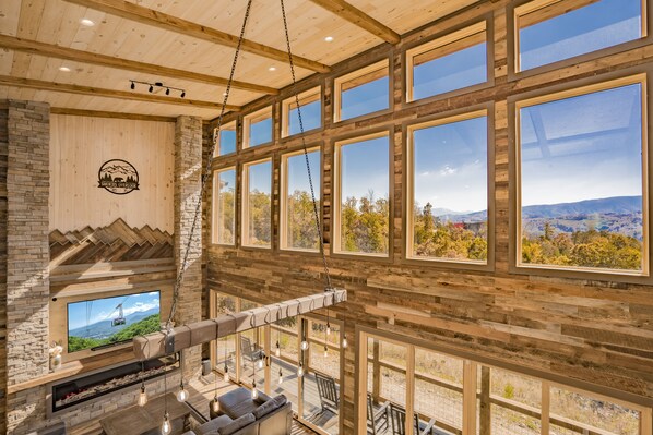 A spacious room with a large TV mounted on a stone wall, wooden beams, and a view of a mountainous landscape.