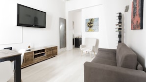 Un salon moderne avec un téléviseur à écran plat, un canapé, un fauteuil blanc et un meuble en bois.