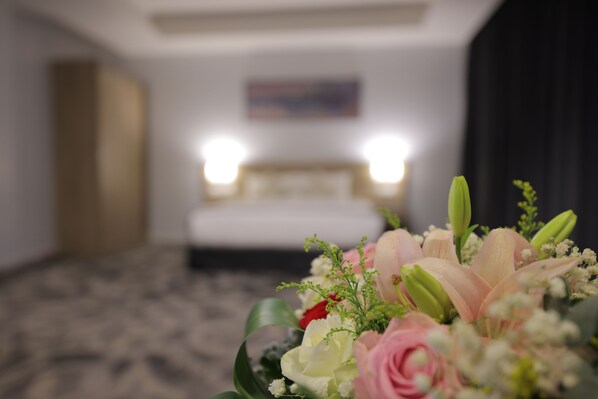 Une chambre d’hôtel avec un lit, une table de chevet et un arrangement floral sur le côté.