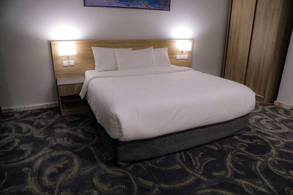 Un lit bien fait, avec une tête de lit en bois, deux lampes de chevet et un tapis à motifs.