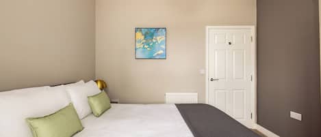 A bedroom with a bed, pillows, a radiator, a door, and a wall-mounted artwork.