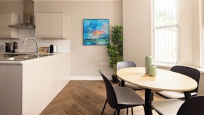 A modern kitchen with white cabinets, a stainless steel sink, and a wooden dining table with chairs.