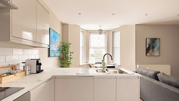 A modern kitchen with a built-in island, a dining area, and a gray sofa.