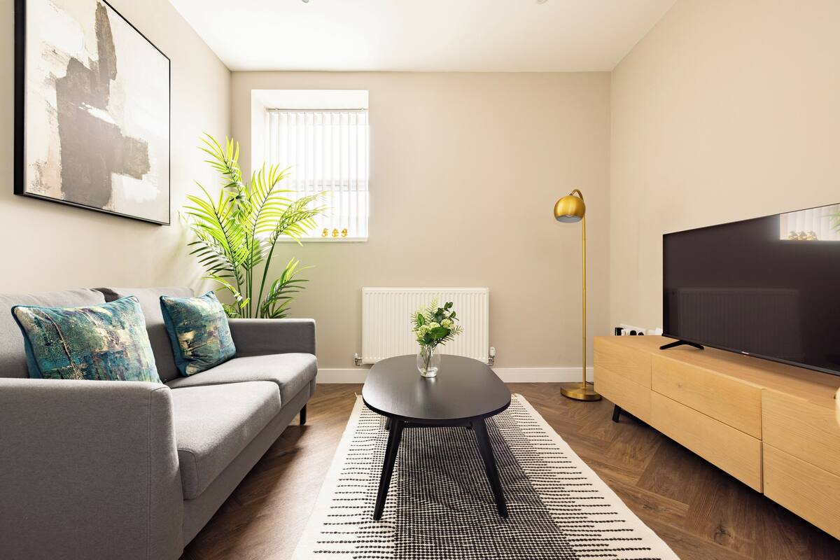 Een moderne woonkamer met een grijze bank, een zwarte salontafel, een houten kast en een grote flatscreen televisie.