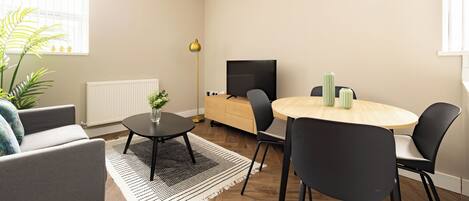 A modern living room with a sofa, a round dining table with chairs, a TV, and a radiator.