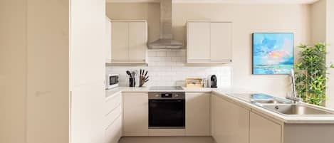 Una cocina moderna con armarios blancos, horno empotrado y pileta.