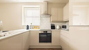 A modern kitchen with white cabinetry, a built-in oven, a microwave, and a stainless steel range hood.