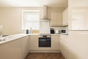 Una cocina moderna con armarios blancos, horno empotrado, microondas y campana extractora de acero inoxidable.
