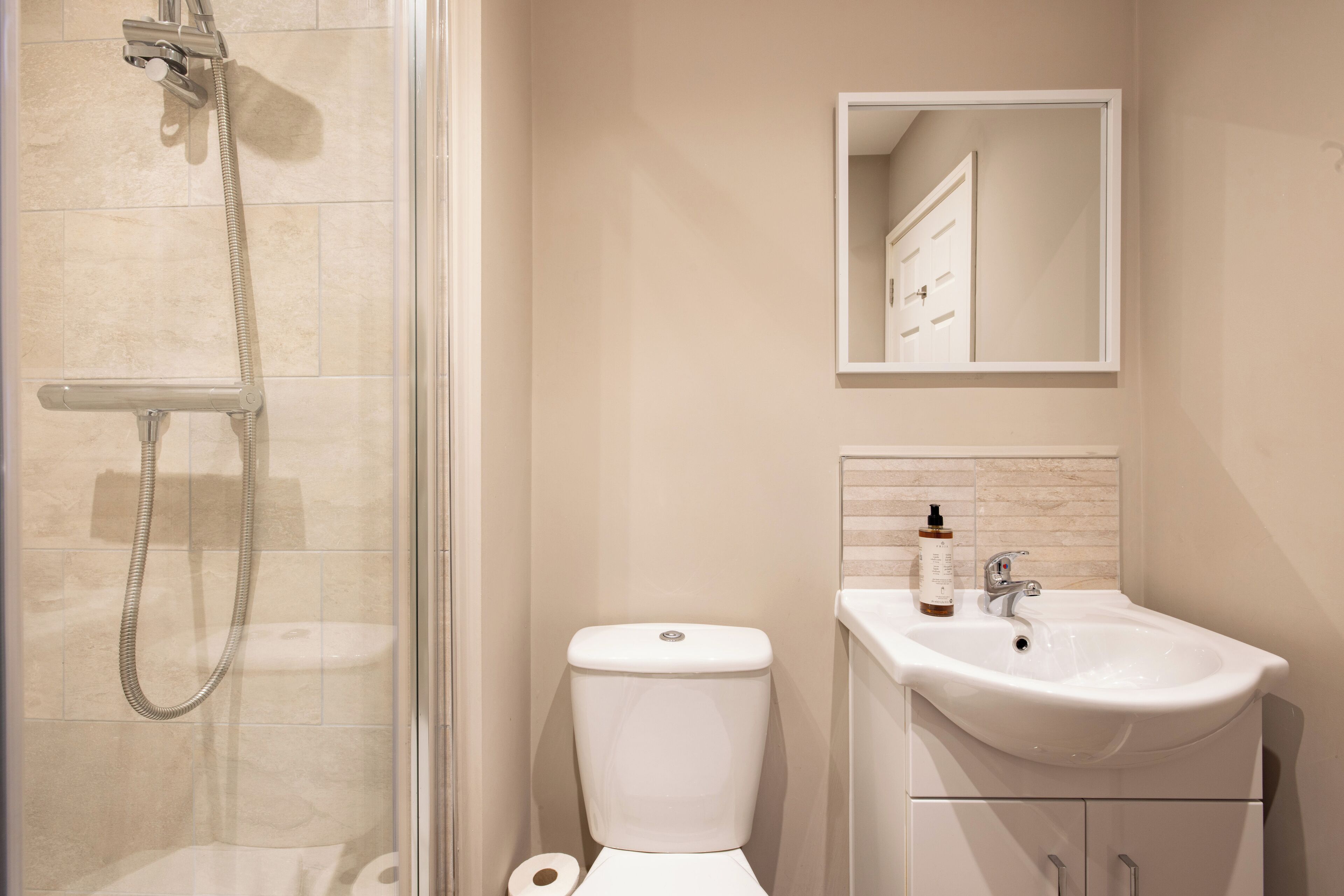 A bathroom with a glass-enclosed shower, a toilet, and a sink with a mirror above it.