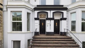 A white building with black-framed doors and windows, a set of stone steps leading to the entrance, and a small black railing on the right side.