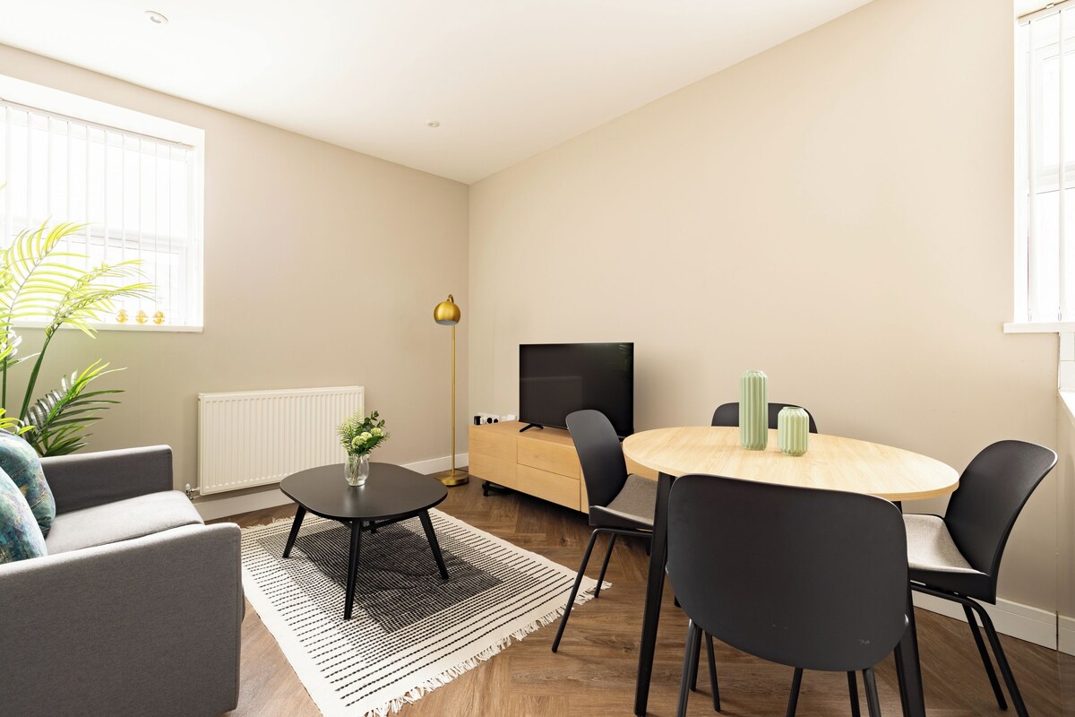 Een moderne woonkamer met een bank, een ronde eettafel met stoelen, een televisie en een radiator.