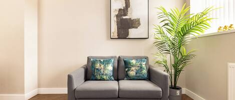 A grey sofa with two blue and white patterned cushions, a round black table, and a potted plant.
