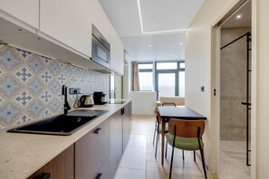 A modern kitchen with a built-in oven, a coffee machine, and a sink. There is a dining area with a table and chairs. - Blue Night International 49 (Paris)