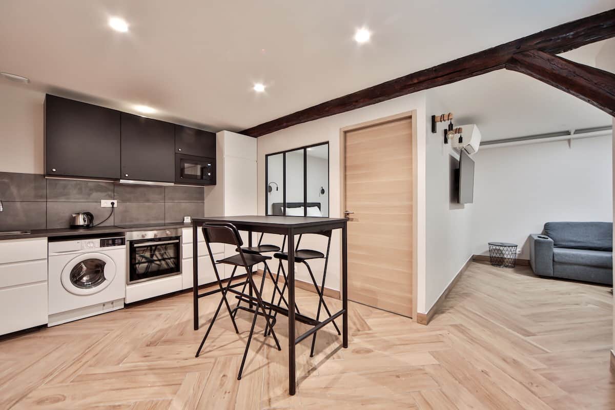 A modern kitchen with dark cabinets, a built-in oven, a washing machine, and a dining area with a table and chairs.