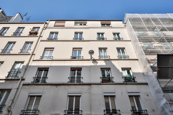 Un edificio de varios pisos con balcones, una antena parabólica y una obra en construcción a la derecha.