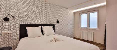 A neatly made bed with white linens, a black headboard, and a geometric patterned wall.
