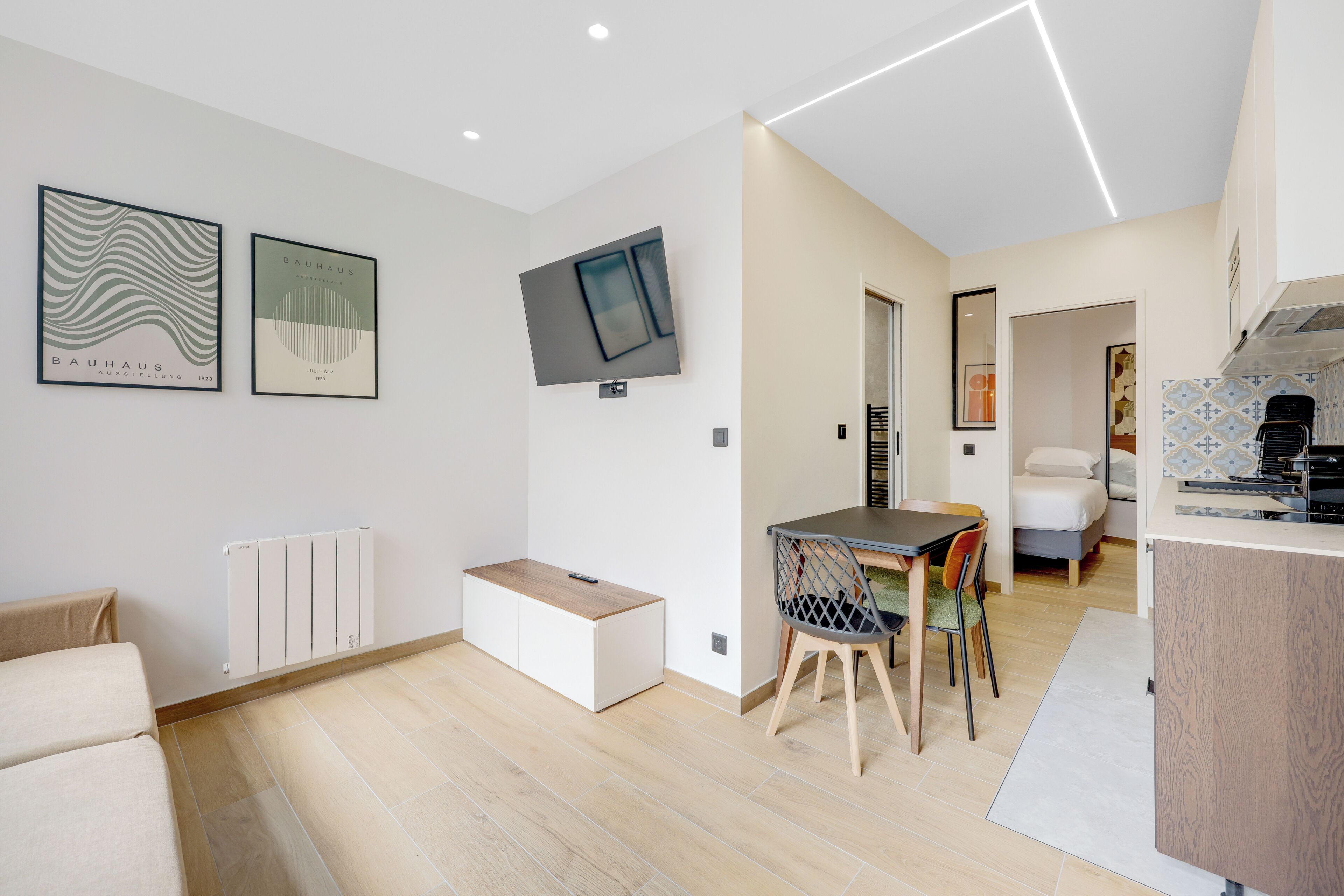 Um espaço moderno com área de jantar, televisão na parede e uma kitchenette.