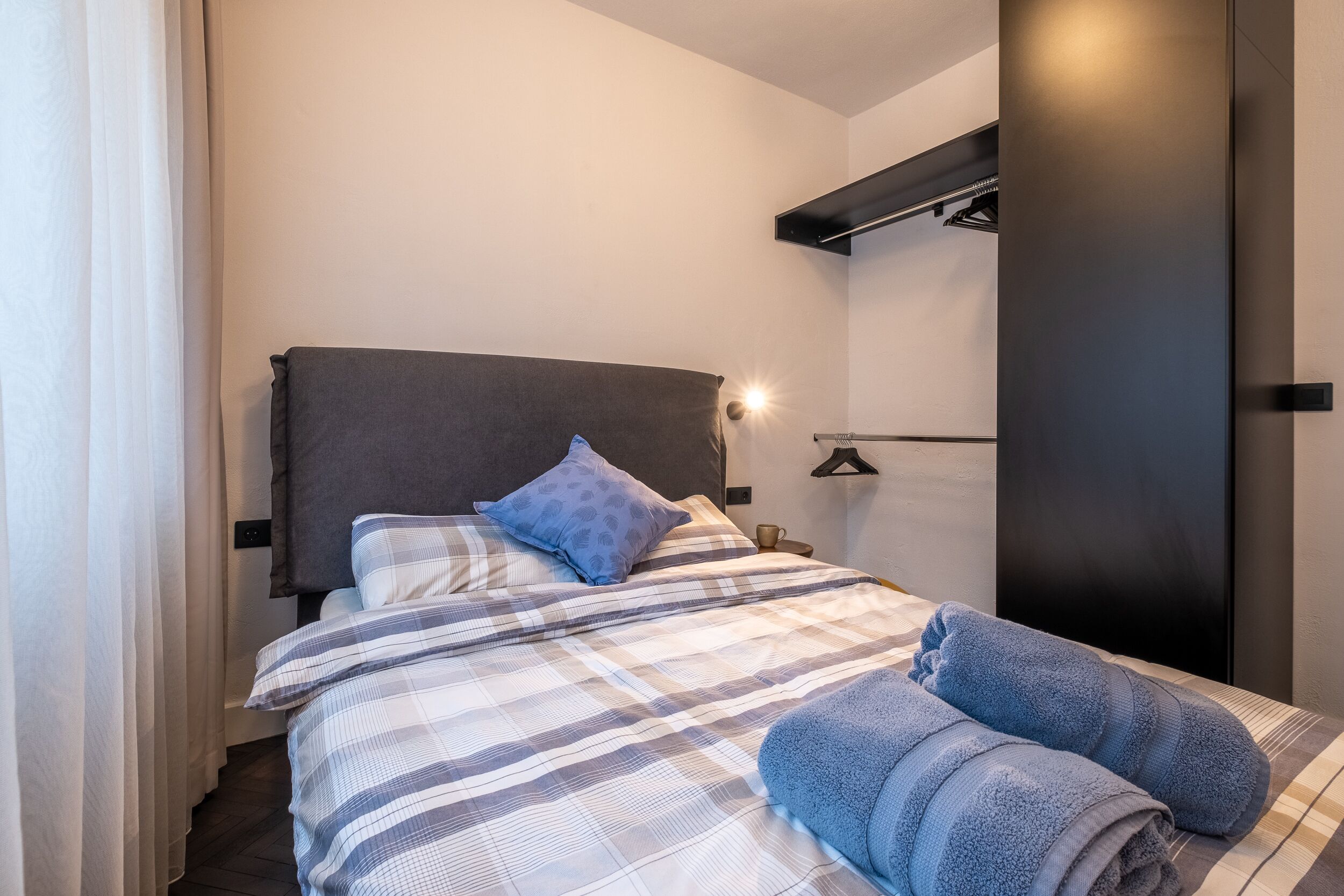 A modern hotel room with a bed, a nightstand, and a wall-mounted light fixture.