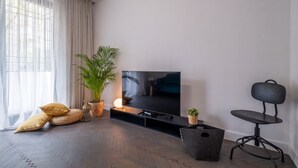 Ein modernes Wohnzimmer mit einem Flachbildfernseher, einer Topfpflanze und einem schwarzen Sessel.