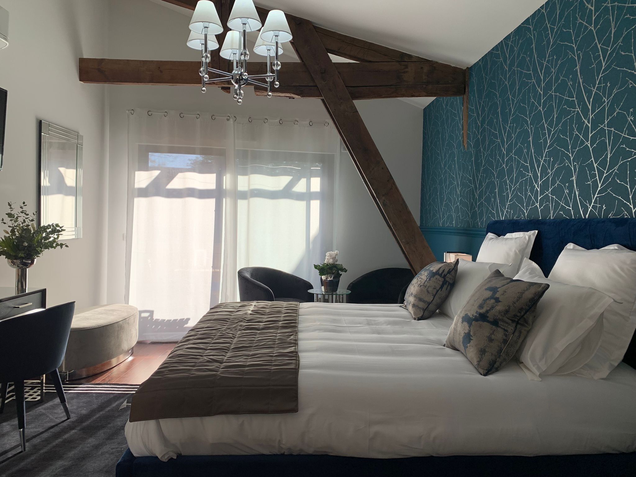 Een slaapkamer met een groot bed, een kroonluchter, een blauwe accentmuur en uitzicht op de omgeving.