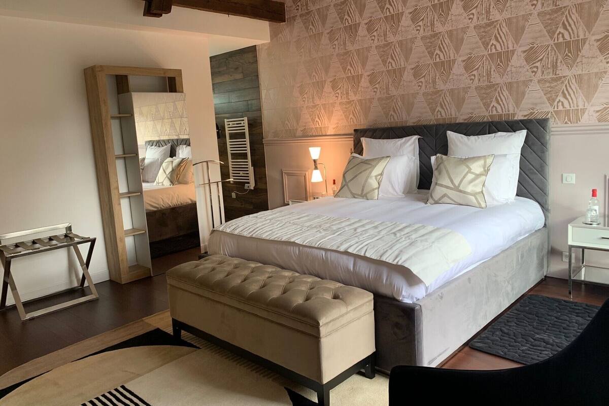 Un dormitorio con una cama grande, un banco de madera, una mesita de noche y un espejo.