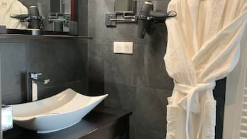 Un baño moderno con un espejo grande, un lavamanos de pedestal, un secador de pelo y una bata colgada en un perchero.