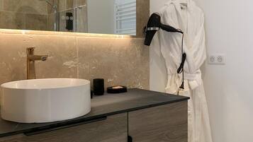 Un baño moderno con un espejo grande, un lavamanos blanco y una bata colgada en un perchero.