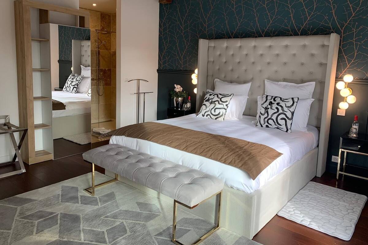Un dormitorio moderno con una cama grande, un banco, un espejo y una mesita de noche con lámpara.