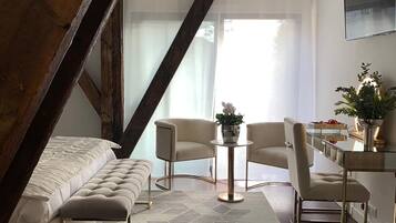 A modern loft bedroom with a sloped ceiling, a large window, a bed, a seating area with chairs, and a small table.