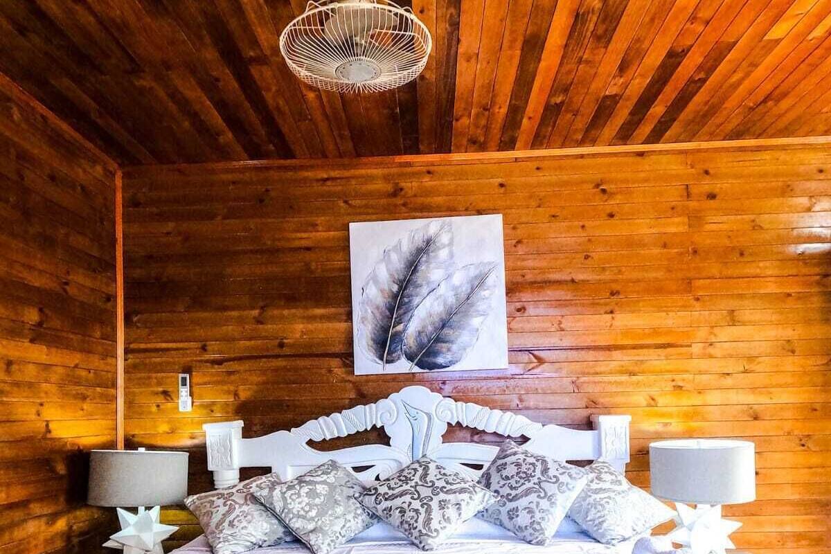 A wooden cabin-style bedroom with a bed, decorative pillows, a feather artwork on the wall, and a ceiling fan.