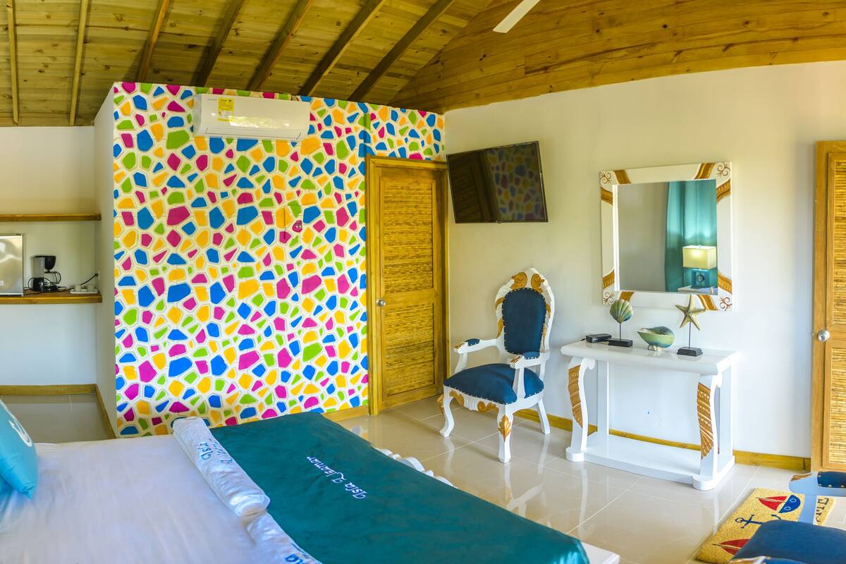 A room with a bed, a desk, a chair, a mirror, and a colorful mosaic wall.