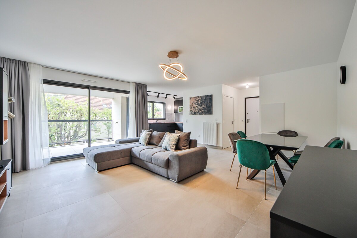 A modern living room with a sectional sofa, a dining table with chairs, and a large window with curtains.