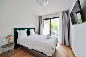 A modern hotel room with a large bed, a bedside table with a lamp, and a view of greenery through the window. - Blue Night International 71 (Saint-Maur-des-Fosses)