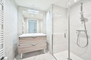 A modern bathroom with a glass shower enclosure, a white sink with a wooden vanity, and a large mirror. - Blue Night International 71 (Saint-Maur-des-Fosses)