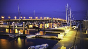 A marina at dusk with boats docked, a bridge in the background, and street lamps along the dock. - Beachfront Retreat | 3-Story Home | Walk to Vilano Beach | Near Nights of Lights (St. Augustine)