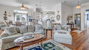 A spacious living room with a large sofa set, a coffee table, and a dining area with chairs. - Beachfront Retreat | 3-Story Home | Walk to Vilano Beach | Near Nights of Lights (St. Augustine)