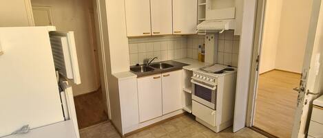 A compact kitchen with white cabinets, a stove, and a sink.