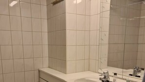 A bathroom with white tiled walls, a large mirror, two sinks, and a shower area.