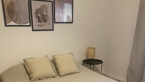 A bedroom with a large bed, two pillows, a small bedside table with a lamp, and three framed artworks on the wall.