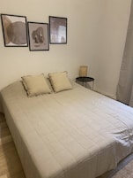 Un dormitorio con una cama grande, dos almohadas, una mesita de noche con lámpara y tres obras de arte enmarcadas en la pared.