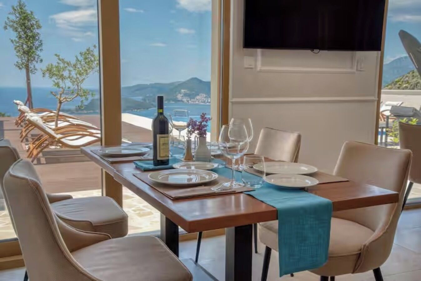 A dining area with a table set for two, a bottle of wine, and a view of the sea and mountains.