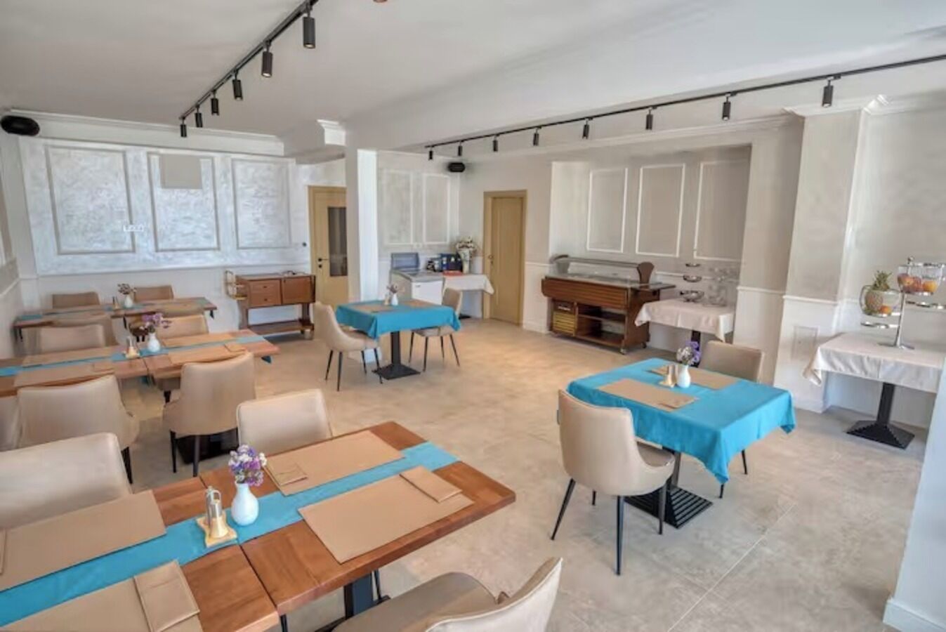 A spacious dining area with multiple tables and chairs, a kitchen area with a counter and appliances, and a view of the adjacent room.