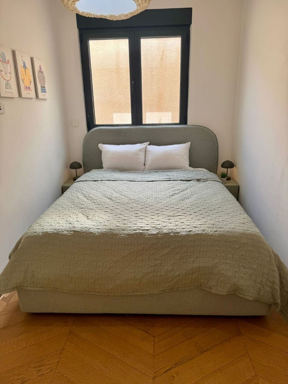 A bedroom with a bed, two bedside tables, a window, and wall art.