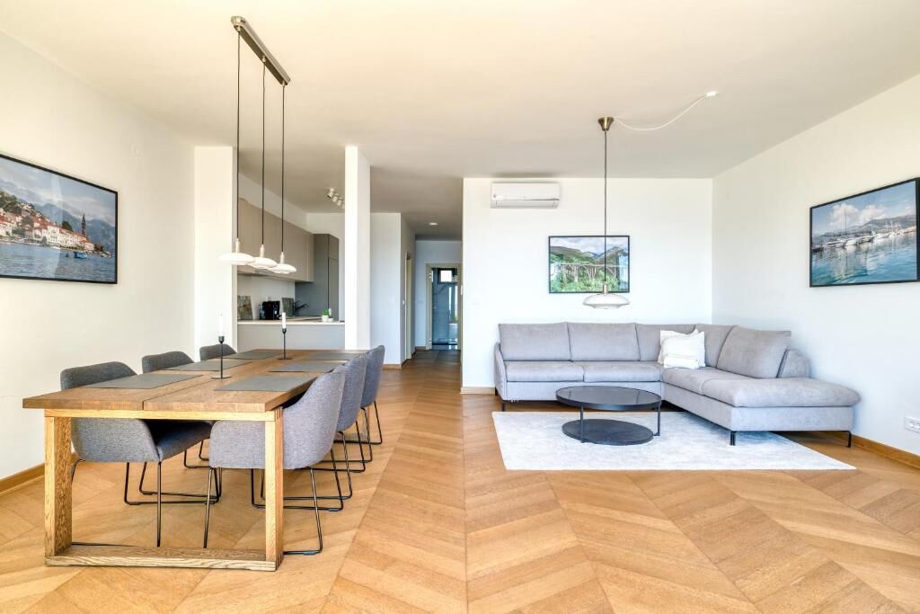 Ein modernes Wohnzimmer mit einem Holzesstisch, einem grauen Sofa und einem großen Fenster.