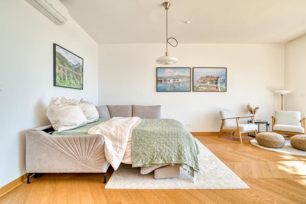 A modern bedroom with a bed, a desk, and two chairs. There are two framed pictures on the wall.