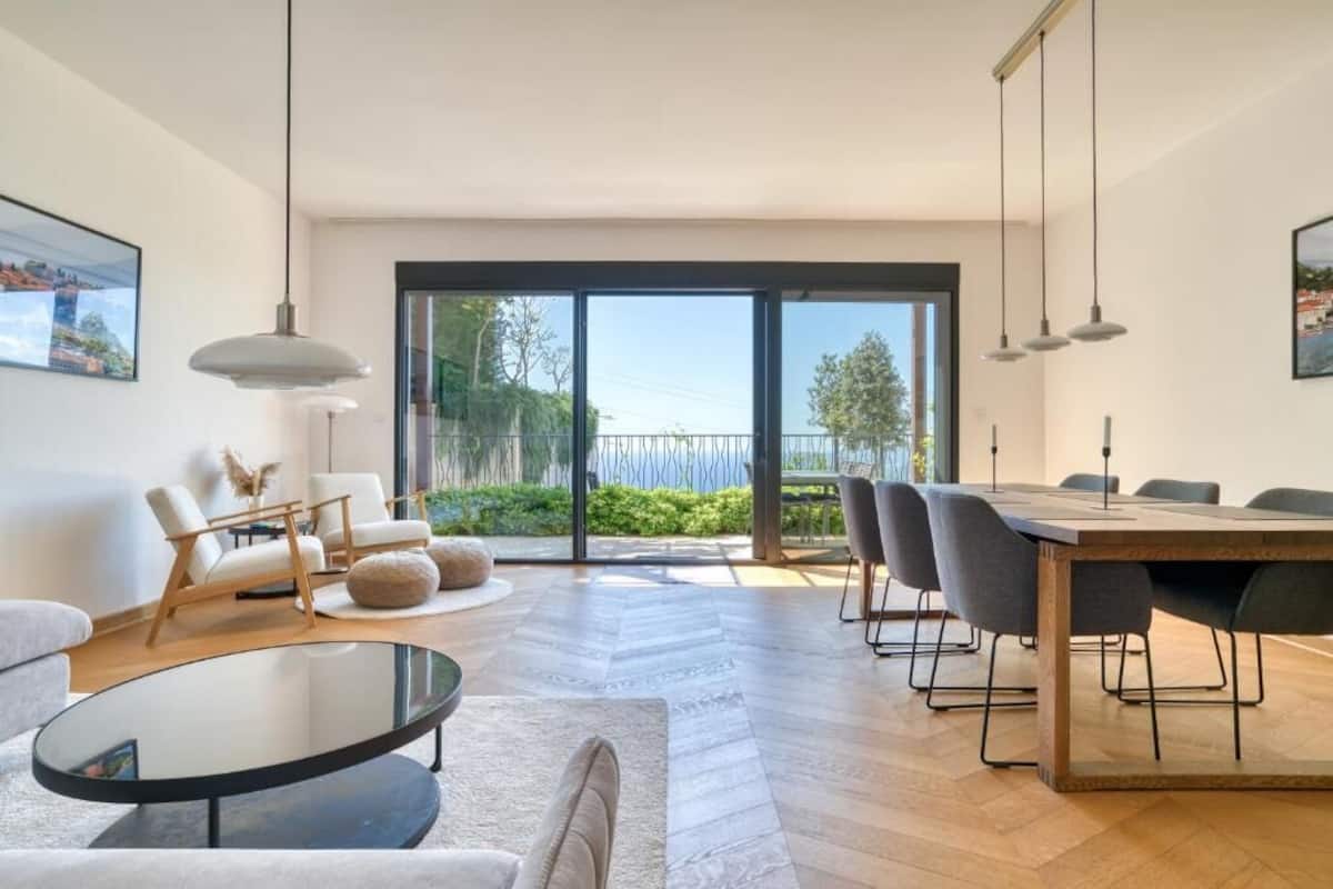 Una sala de estar moderna con una mesa de centro de vidrio, un sofá y un comedor con una mesa y sillas de madera.
